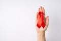 First person top view photo of young woman`s hand holding red silk ribbon in palm symbol of aids awareness on white