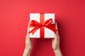 First person top view photo of young woman`s hands holding big white gift box with red ribbon bow on isolated red background Royalty Free Stock Photo