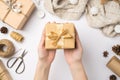 First person top view photo of young woman`s hands holding craft paper giftbox with gold ribbon bow over sweater christmas tree Royalty Free Stock Photo