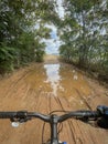 first person view of the handlebars of a mountain bike just before crossing a large puddle of mud and water on a path through a Royalty Free Stock Photo