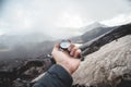 A first-person view of a man`s hand holding a magnetic compass against a background of Caucasus mountains and a cracked Royalty Free Stock Photo