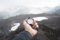 A first-person view of a man`s hand holding a magnetic compass against the background of the snow-capped mountains of Royalty Free Stock Photo