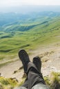 A first-person view POV of a man sits on the edge of a high cliff and enjoys the scenery. Wide angle human foot trekking Royalty Free Stock Photo