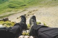 A first-person view POV of a man sits on the edge of a high cliff and enjoys the scenery. Wide angle human foot trekking Royalty Free Stock Photo