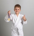 First place award. Boy in white kimono with gold furniture in hand. Satisfied child shows thumbs up. Gray background