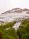 First snow in Alps touristic region. Fresh green meadow with rapids stream. Peaks of Alps mountains in background.