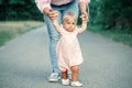 First steps of baby. Cute baby girl learning to walk and holding her mother hand. Mom helping toddler child daughter to go in park Royalty Free Stock Photo