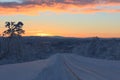 The first sun rays on the road in the snow-covered Northern winter forest after the polar night Royalty Free Stock Photo
