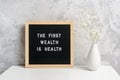 The first wealth is health. Motivational quote on letter board and bouquet of flowers gypsophila in vase on table against stone
