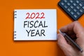 2022 fiscal new year symbol. Businessman writing words `2022 fiscal year` on white note. Black calculator. Beautiful orange