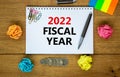 2022 fiscal new year symbol. White note, words 2022 fiscal year on beautiful wooden table, colored paper, colored pencils, paper