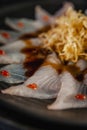 Fish carpaccio in a black plate with sweet potato straws