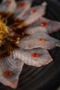 Fish carpaccio in a black plate with sweet potato straws