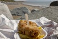 Fish and chips, battered cod, in a tray wrapped in paper with a wooden fork on a beach. Traditional British food Royalty Free Stock Photo