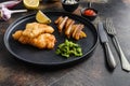 fish and chips with beer-battered cod and fries and a side of tartar sauce and mushy peas on black plate over old rustic metal Royalty Free Stock Photo