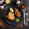 Fish and chips with beer-battered cod and fries and a side of tartar sauce and mushy peas on black plate over old rustic metal Royalty Free Stock Photo