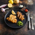 Fish and chips with beer-battered cod and fries and a side of tartar sauce and mushy peas on black plate over old rustic metal Royalty Free Stock Photo