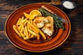 Fish and Chips british fast food with french fries and tartar sauce on a rustic plate. Dark wooden background. Top view Royalty Free Stock Photo