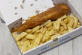 Fish and chips in a cardboard box from a takeaway.  Grey wood background Royalty Free Stock Photo