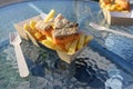 Fish and chips with fried smoked salmon and french fries in a cardboard box and a wooden fork on a glass table, fast food in an