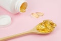 Fish Gelatin Softgels Omega-3 in wooden spoon and open white plastic jar with capsules on a pink background