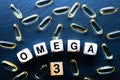 Fish oil pills and wooden cubes with inscription OMEGA 3 on a dark background, top view