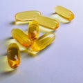 Fish oil. Yellow softgels or capsules lie on purple surface. Square illustration about vitamins and healthy lifestyle. Softgel
