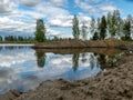 A fish pond, in the water of which there are colorful cumulus clouds and trees, there are recently dug gravel piles on the shore