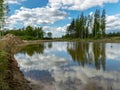 A fish pond, in the water of which there are colorful cumulus clouds and trees, there are recently dug gravel piles on the shore