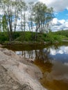 A fish pond, in the water of which there are colorful cumulus clouds and trees, there are recently dug gravel piles on the shore