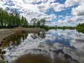 A fish pond, in the water of which there are colorful cumulus clouds and trees, there are recently dug gravel piles on the shore