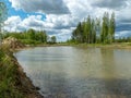 A fish pond, in the water of which there are colorful cumulus clouds and trees, there are recently dug gravel piles on the shore