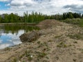 A fish pond, in the water of which there are colorful cumulus clouds and trees, there are recently dug gravel piles on the shore