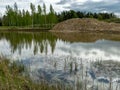 A fish pond, in the water of which there are colorful cumulus clouds and trees, there are recently dug gravel piles on the shore