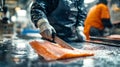 A fish processing worker in protective gear skillfully cuts fish with an electric fillet knife, surrounded by industrial machinery Royalty Free Stock Photo