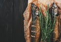 Fish with rosemary on parchment paper on a black wooden background, healthy food on kitchen table top view, grill seafood