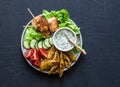 Fish skewers, baked potatoes, vegetables and yogurt greens sauce on dark background, top view Royalty Free Stock Photo