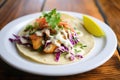 fish taco with cabbage slaw and white sauce on a corn tortilla