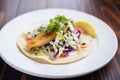 fish taco with cabbage slaw and white sauce on a corn tortilla