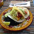 Fish tacos on a colorful plate with black beans and lime.