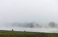 Fisher man fishing on a river bank at misty foggy sunrise