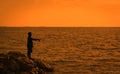 Fisher man fishing with spinning rod on a sea . Young men Fishing in the reservoir At sunset .
