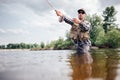 Fisherman in action. Guy is throwing spoon of fly rod in water and holding part of it in hand. He looks straight forward Royalty Free Stock Photo