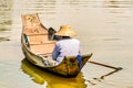 Fisherman in an Asian cone hat sailing in the lake with a small wooden boat