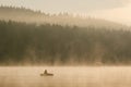 A fisherman in a boat catches fish in the early foggy morning and the forest in the distance Royalty Free Stock Photo