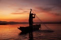 Fisherman casting his net on during sunset. Silhouette Asian fisherman on wooden boat casting a net for freshwater fish. Royalty Free Stock Photo