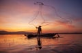 Fisherman casting his net on during sunset. Silhouette Asian fisherman on wooden boat casting a net for freshwater fish. Royalty Free Stock Photo