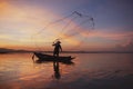 Fisherman casting his net on during sunset. Silhouette Asian fisherman on wooden boat casting a net for freshwater fish. Royalty Free Stock Photo