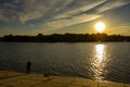 A fisherman catches fish from the shore of a modern city at sunset