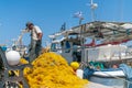 Fisherman checks and mends bright yellow fishing nets on wharf